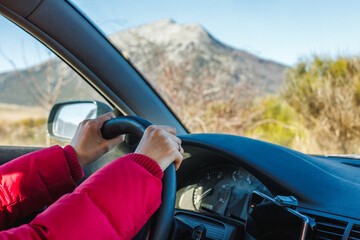 Woman hands holding steering wheel with mountains in the background