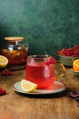 Hot drink, tea with viburnum and citrus in a transparent glass mug on a wooden background. Autumn warming drinks