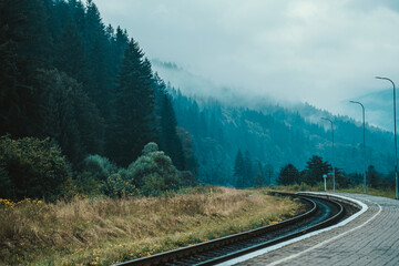 Scenic view of winding railway tracks through misty forests in the mountains on a cloudy day