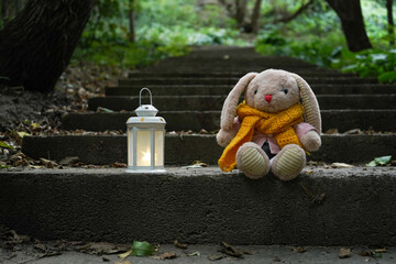 Toy hare sits on stone stairs in the forest in cloudy weather in autumn