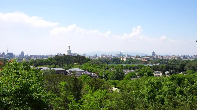 Zoom in shot to Beihai White Tower seen from a lush green hilltop with Beijing skyline in the distance, China