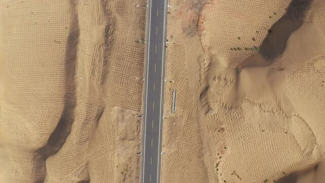 Top-down view of a highway in the Gobi Desert, lined with sand fences for protection. Sand dunes along an empty road in Inner Mongolia. Arid landscape. Road infrastructure in a desert environment.