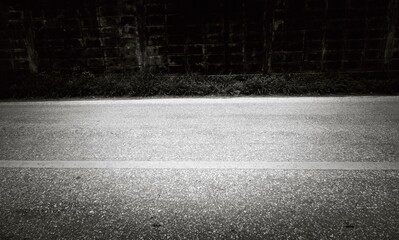 Fototapeta premium A road with a white line and a brick wall in the background. The road is empty and the sky is dark