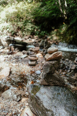 Obraz premium Stacked stones along a serene riverbank in a lush forest setting during a sunny afternoon