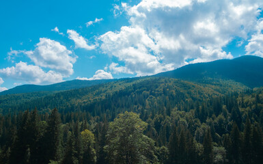 Lush green mountains under bright blue sky with fluffy white clouds during a sunny day in a tranquil landscape