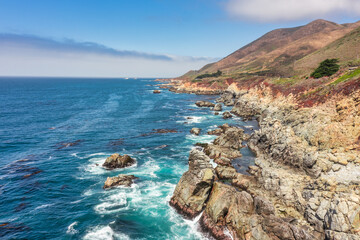 Fototapeta premium Beautiful landscape of Pacific Ocean coast along Highway 1 and Big Sur, aerial view, sunset, sunrise, fog. Concept, travel, vacation, weekend