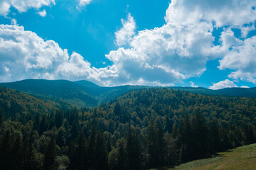 Scenic view of rolling hills and dense forests under a bright blue sky with fluffy white clouds during a sunny day in the mountains