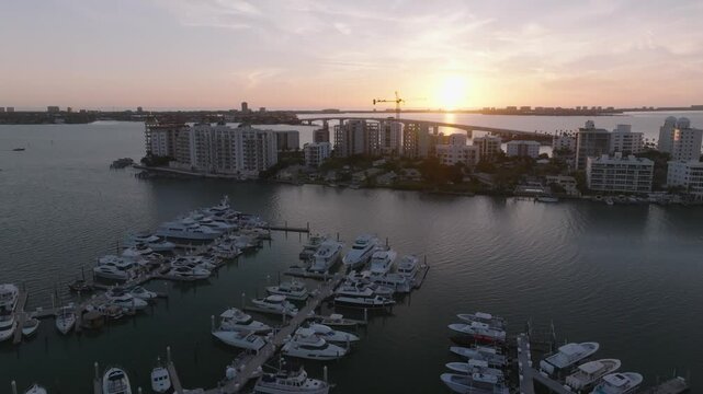 Drone footage of Freedom Boat Club at Sarasota Marina Jack and Bayfront Park at sunset. Shows docked boat, Sarasota Bay, condos, construction crane, and the John Ringling Causeway and Bridge.