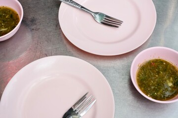 Distinctive pastel pink plastic plates and bowls of nam jim jaew (seafood dipping sauce) on metal tables at Somsak Pu Ob (Charoen Rat) a street food cart in Khlong San - Bangkok, Thailand