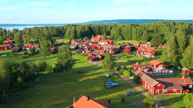 Village in Sweden with red house in drone shot. Aerial view green forest and typical wooden cabins. Afternoon light by calm lake on warm beautiful summer day. Dalarna historical central Sweden.