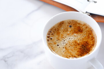 ミルクをたっぷり入れたコーヒーを飲みながら、茶色の革のシステム手帳でデスクワークをしているイメージ
