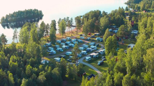 Camping ground in the forest by lake at sunset. Aerial drone flight. Light fading through green trees. Dream like cinematic shot of campsite in Sweden or Norway Scandinavia