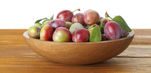 Fresh plums and green leaves in bowl on wooden table against white background