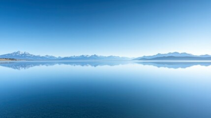 A clear blue sky over a tranquil lake, with distant mountains reflecting perfectly on the calm water.