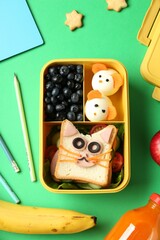 Lunch box with snacks, bottle of juice and stationery on green table, flat lay