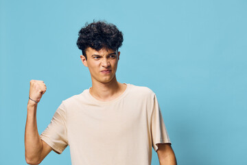 Young man expressing anger with a clenched fist on a solid blue background, showcasing a strong...