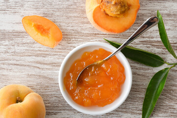 Peach jam in a bowl and pieces of fruit around