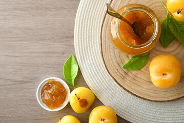 Jar filled with plum jam on wood cutting board