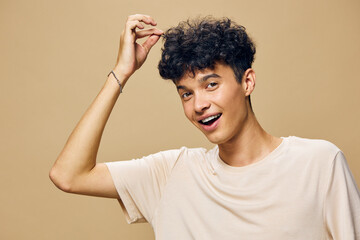 Young man with curly hair smiling on a beige background, showing a playful expression while touching his hair A warm and inviting atmosphere is created by the soft tones