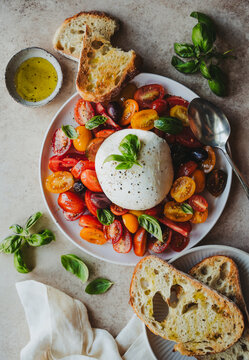 Overhead of plates of burrata cheese, tomatoes, basil and bread.