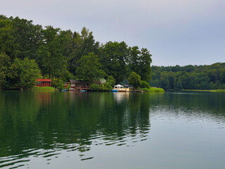 Obraz premium Malerische Fernsicht auf das bewaldete Seeufer mit kleinen Ferienhäusern und Spiegelungen auf der Wasseroberfläche, Liepnitzsee, Landkreis Barnim, Brandenburg, Deutschland
