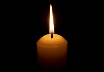 A single burning candle flame or light glowing on a big white candle isolated on red or dark background on table in church for Christmas, funeral or memorial service