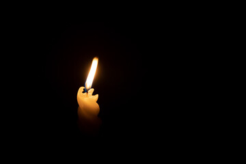 A single burning candle flame or light glowing on a spiral white candle on black or dark background...