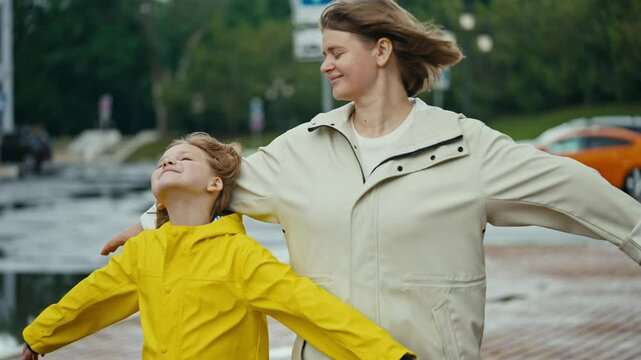Happy blonde woman together with her teenage daughter girl in a yellow jacket stand against the wind and enjoy the wind while walking in the park after the rain