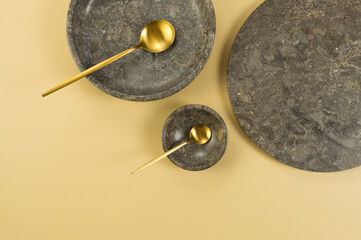 Top view of brown marble tray, plate, bowl and gold cutlery on yellow background. Food presentation, dishes, stone tray. Copy space, flat lay.