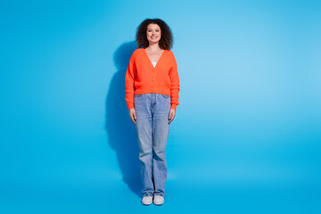 Photo portrait of wavy haired model woman wearing orange cardigan and jeans stylish outfit isolated on blue color background