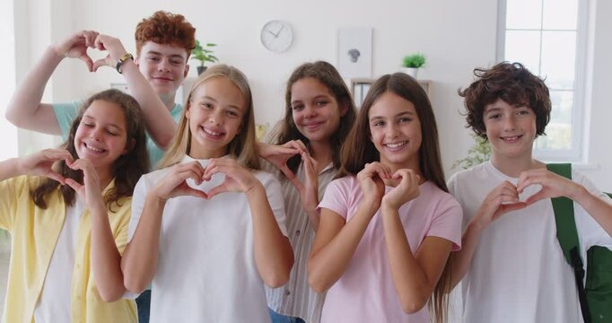 School student friends and classmates girls and boys standing together, looking at camera, smiling, promoting friendly educational environment, showing heart gesture of loving team communication