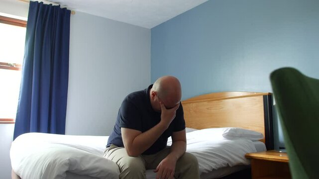 A desperate lonely man crying sitting on a bed with his head in his hand, appearing distressed or overwhelmed. Emotion or struggle after a divorce.