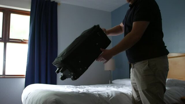 A lonely man arriving and entering a hotel or motel room unzipping and unpacking a suitcase bag. A moment of travel or transition