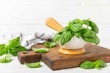 Fresh green basil in a mortar on a textured wooden background. Organic spices and herbs. Vegan. Fresh kitchen herbs. Fresh basil being made into pesto with mortar and pestle.Copy space. Place for text