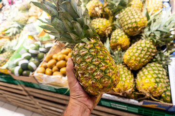 A person is holding a pineapple in a grocery store