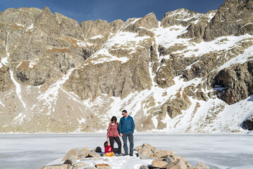 Family with one child at a frozen pyrenean lakeshore called Ibón del Sen in Chistau Valley.