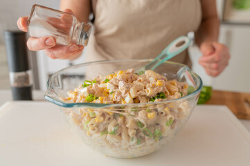 Woman salting a fresh and homemade pasta tuna salad in the kitchen