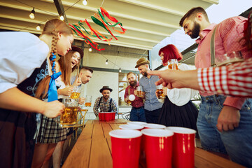 Group of people meeting at pub for beer festival celebration, having fun and playing beer pong. Concept of Oktoberfest, festival, party, brewery, traditions
