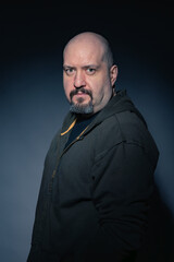 Obraz premium Mature bald man with goatee, dressed in black casual clothes on black background looking at camera with serious expression. Studio photography. Concept of man, maturity and baldness