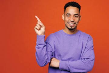 Young happy man of African American ethnicity wear purple sweatshirt casual clothes point index finger aside on area mockup isolated on plain red orange background studio portrait. Lifestyle concept.