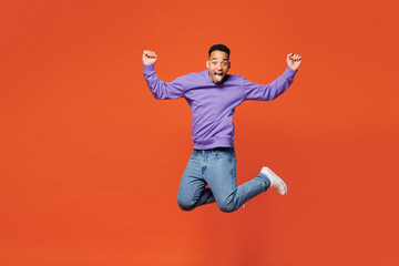 Obraz premium Full body young happy cool man of African American ethnicity wear purple sweatshirt casual clothes jump high do winner gesture clench fist isolated on plain red orange background. Lifestyle concept.