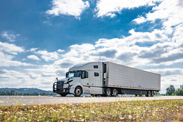 Long haul white big rig semi truck with grille guard transporting cargo in refrigerator semi...