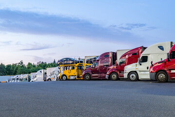 Professional industrial big rigs semi trucks with different semi trailers standing in row on truck...