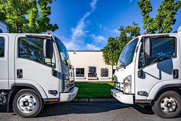 Two small over cab rigs semi trucks with extended cabs and box trailers standing opposite each...