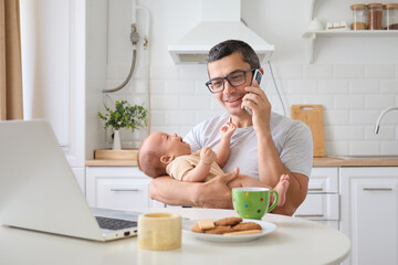 Satisfied cheerful man father talking on smartphone holding baby in kitchen managing business call...