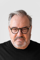 Erwachsener Mann mit grau schwarz meliert Bart in einem schwarzen T-Shirt im Portrait, lächelt in die Kamera, sympathisch, mit einer schwarz umrandete Brille