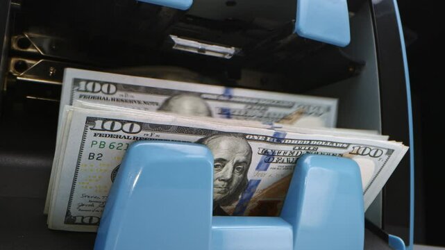 Counting cash at a bank ATM in the city during the afternoon on a busy weekday morning