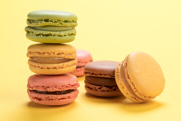 Variety of pastel colored french macarons pastry on light yellow background