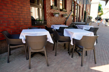 Fototapeta premium Empty sidewalk cafe with chairs, tables with white tablecloth. Empty tables and chairs with white tablecloths on serene outdoor terrace of summer restaurant, peaceful setting