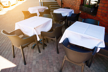 Empty summer restaurant terrace with white tablecloths on tables and chairs, showcasing an elegant outdoor setting perfect for alfresco dining and relaxation.
